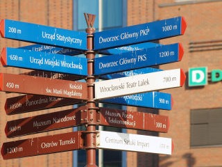 Poste de señalización urbana con múltiples direcciones en diferentes colores, facilitando la orientación en un área turística o comercial.